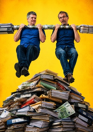 Die beiden Mitglieder der Reading Heads machen einen Klimmzug an einer mit Geld umwickelten und mit Akten beschwerten Stange- Im Hintergrund ist ein Haufend bestehend aus Akten und 100-Euro-Scheinen zu sehen.